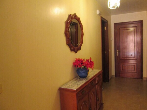 A hallway with a wooden door, a mirror, and a vase with red flowers on a marble counter.