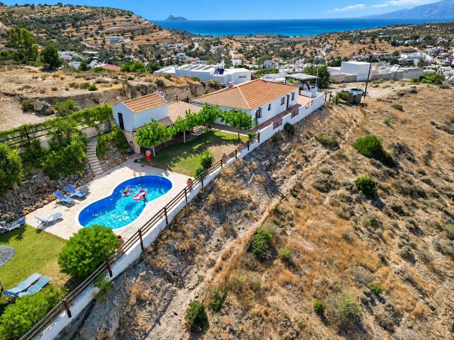 A residential area with a swimming pool, white houses, and a view of the sea.