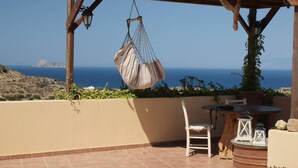 A patio with a hanging chair, a table, and a view of the sea. - Villa with sea and mountain views, private pool and large garden (Pitsidia)