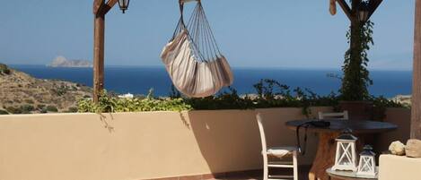 Eine Terrasse mit einer Hängesitzgelegenheit, einem Tisch und Blick auf das Meer.
