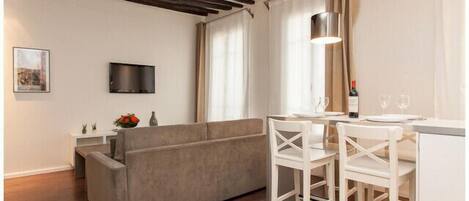 Un salon moderne comprenant un canapé, un téléviseur, un coin repas avec des chaises et un comptoir de cuisine.