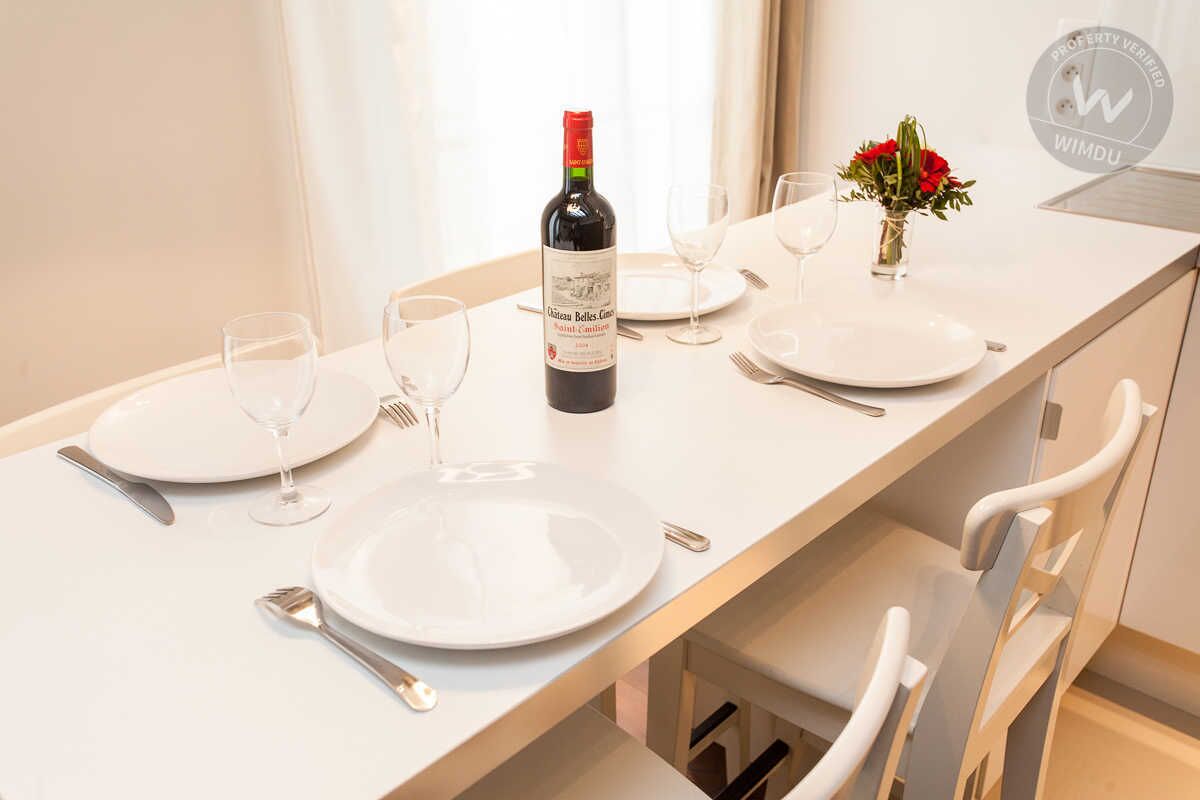 A dining table set with white plates, cutlery, and wine glasses, with a bottle of wine and a vase of flowers.