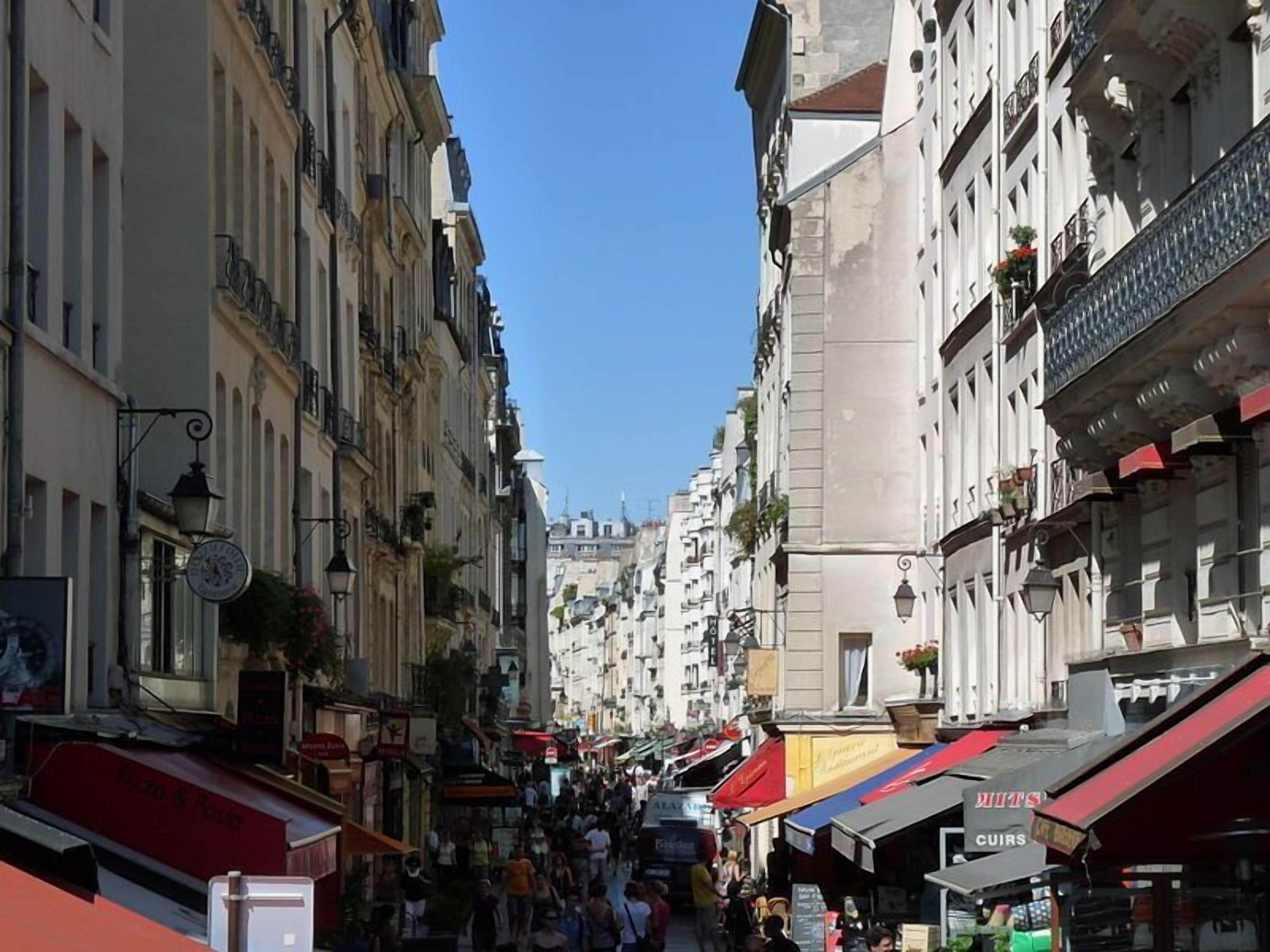 Une rue animée bordée de bâtiments historiques, de boutiques et de cafés, ce qui témoigne d’une atmosphère urbaine dynamique.