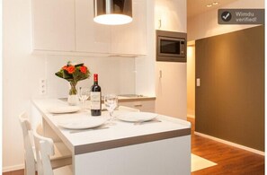 Una cocina moderna con armarios blancos, microondas integrado y un comedor con platos blancos y una botella de vino.