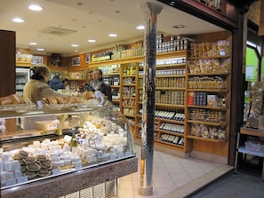 Una panadería con un expositor de vidrio lleno de pasteles y pan, estantes repletos de productos horneados y artículos envasados, y una decoración de madera.