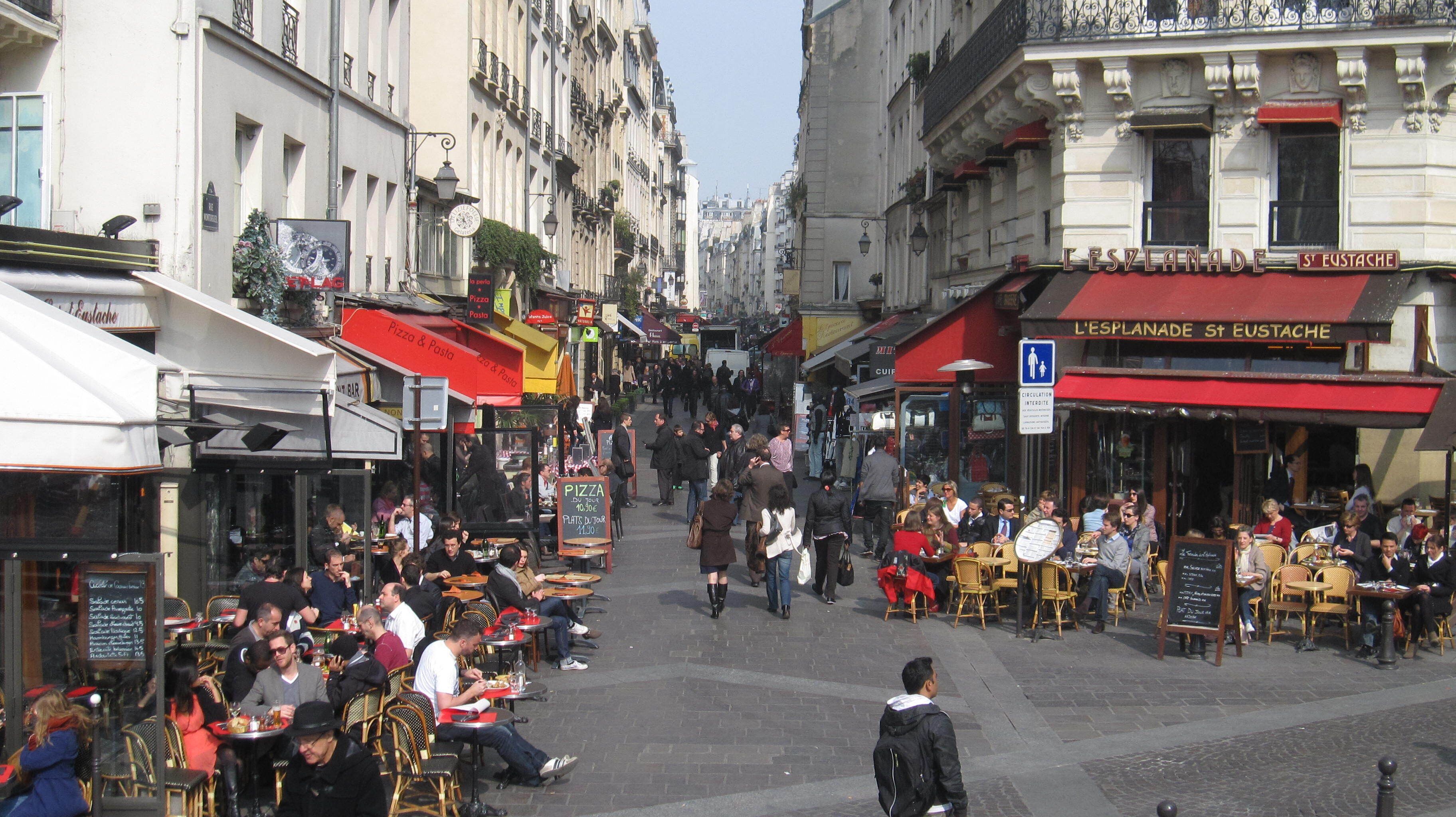 Een levendige straat met terrassen bij cafés en restaurants.