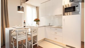 A modern kitchen with white cabinetry, a built-in microwave, and a dining area with white chairs and a table.