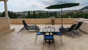 A terrace with a table and chairs, a potted plant, and a view of a town and hills in the distance. - Penthouse. 4 pers. Private Solarium Terrace 105m2, pool 12 m by 6 (Saint-Paul-De-Vence)