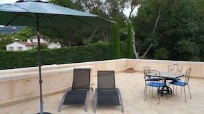 Une terrasse extérieure avec une table et des chaises, un parasol vert et une vue sur une maison et des arbres.