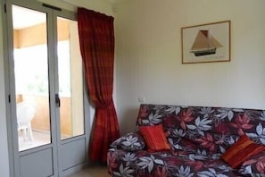 Une pièce comprenant un canapé, un tableau encadré représentant un voilier et une porte-fenêtre coulissante donnant sur un espace extérieur.