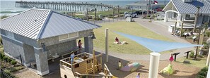 Un parque infantil con tobogán y estructuras para escalar, un área de descanso cubierta y vistas al océano.