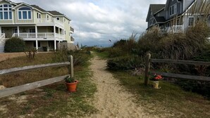 Een pad dat leidt naar een strandpand met een gebouw van twee verdiepingen, voorzien van balkons en een zandstrand.
