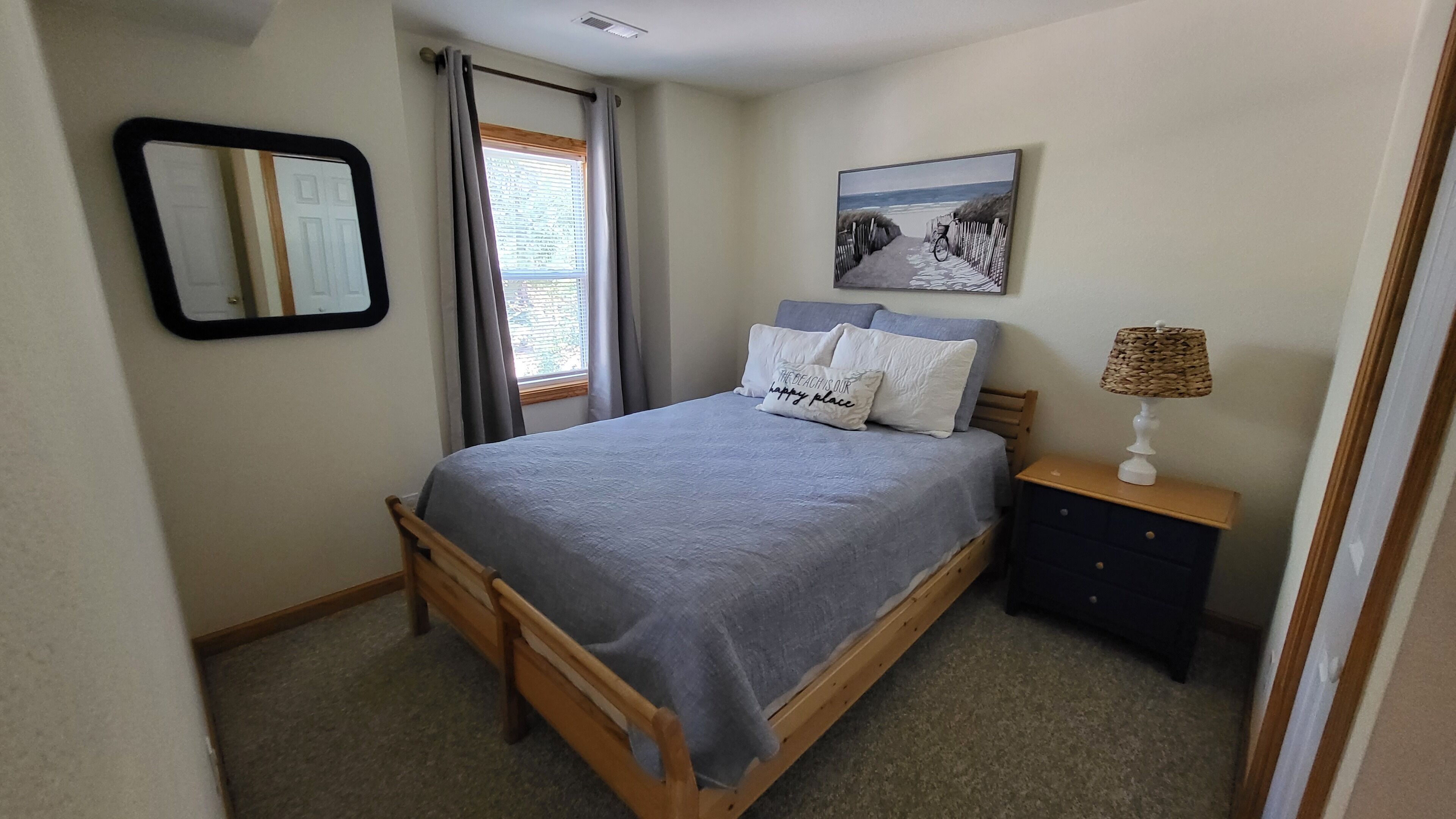 A bedroom with a bed, a nightstand, a lamp, a mirror, and a window with curtains.