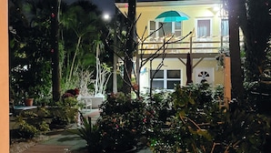 Un edificio bien iluminado con balcón y un patio con plantas en macetas y una poinsettia roja.