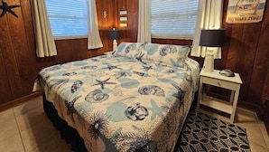 Un dormitorio con cama, dos lámparas de noche, una decoración con forma de estrella de mar y paneles de madera, además de un letrero que indica 'No Wake Zone'.