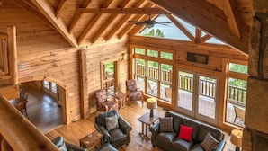 Eine geräumige Holzhütte mit hohen Decken, einem Essbereich, einem Wohnzimmer mit Ledermöbeln und großen Fenstern mit Blick ins Freie.