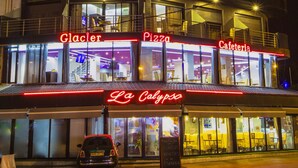 Un edificio de varios pisos con letreros iluminados que dicen 'Glacier', 'Pizza' y 'Café'.