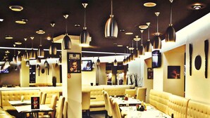 Interior de un restaurante con varios asientos tipo cabina y mesas, iluminación colgante y televisores en la pared.