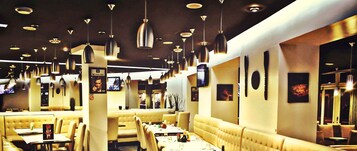 A restaurant interior with multiple booths and tables, pendant lighting, and wall-mounted televisions.
