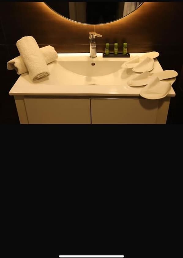 A bathroom with a white sink, a mirror, and toiletries. - Calypso Home (Ain El Turk)