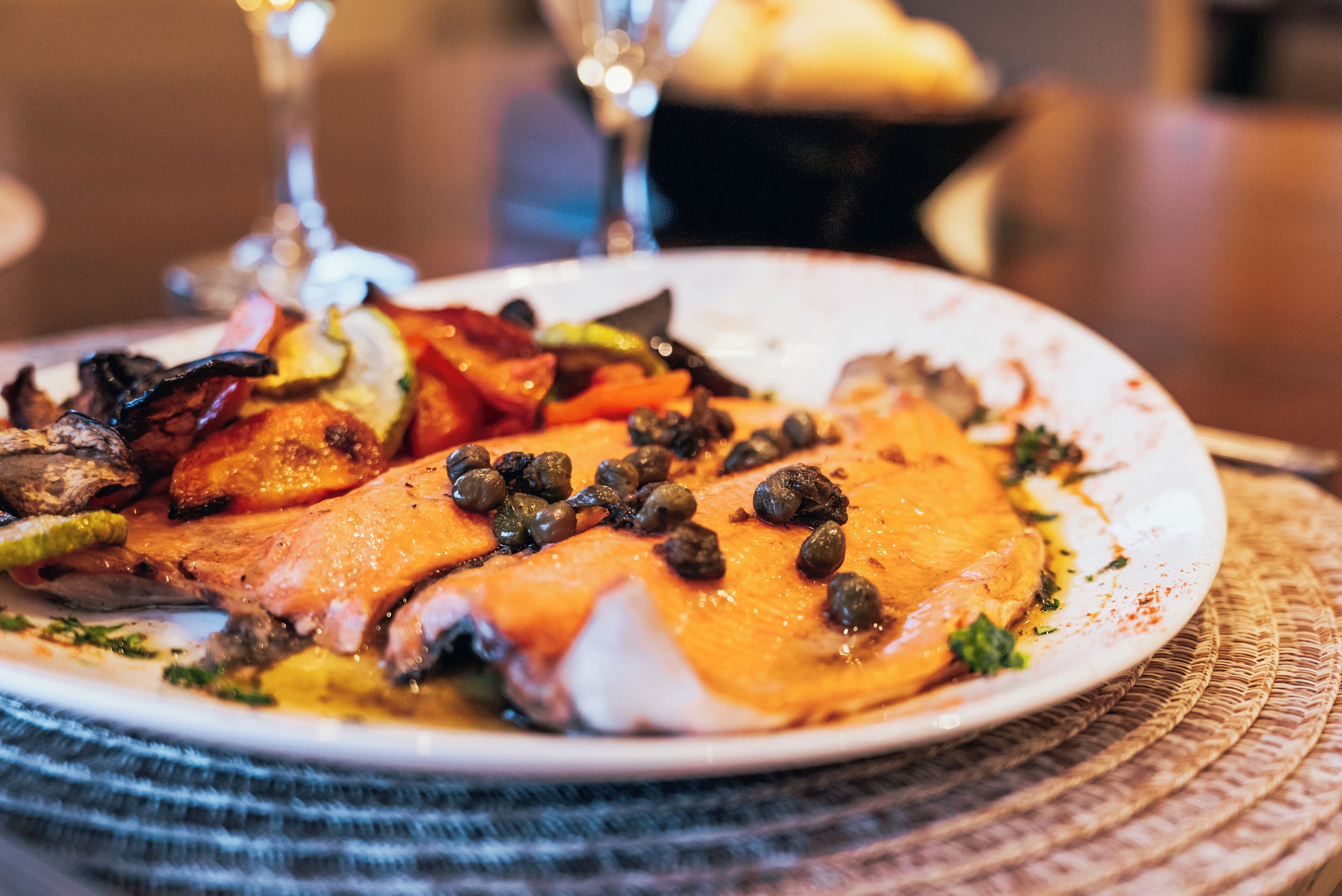 Une assiette de nourriture comprenant du saumon, des légumes et des câpres.