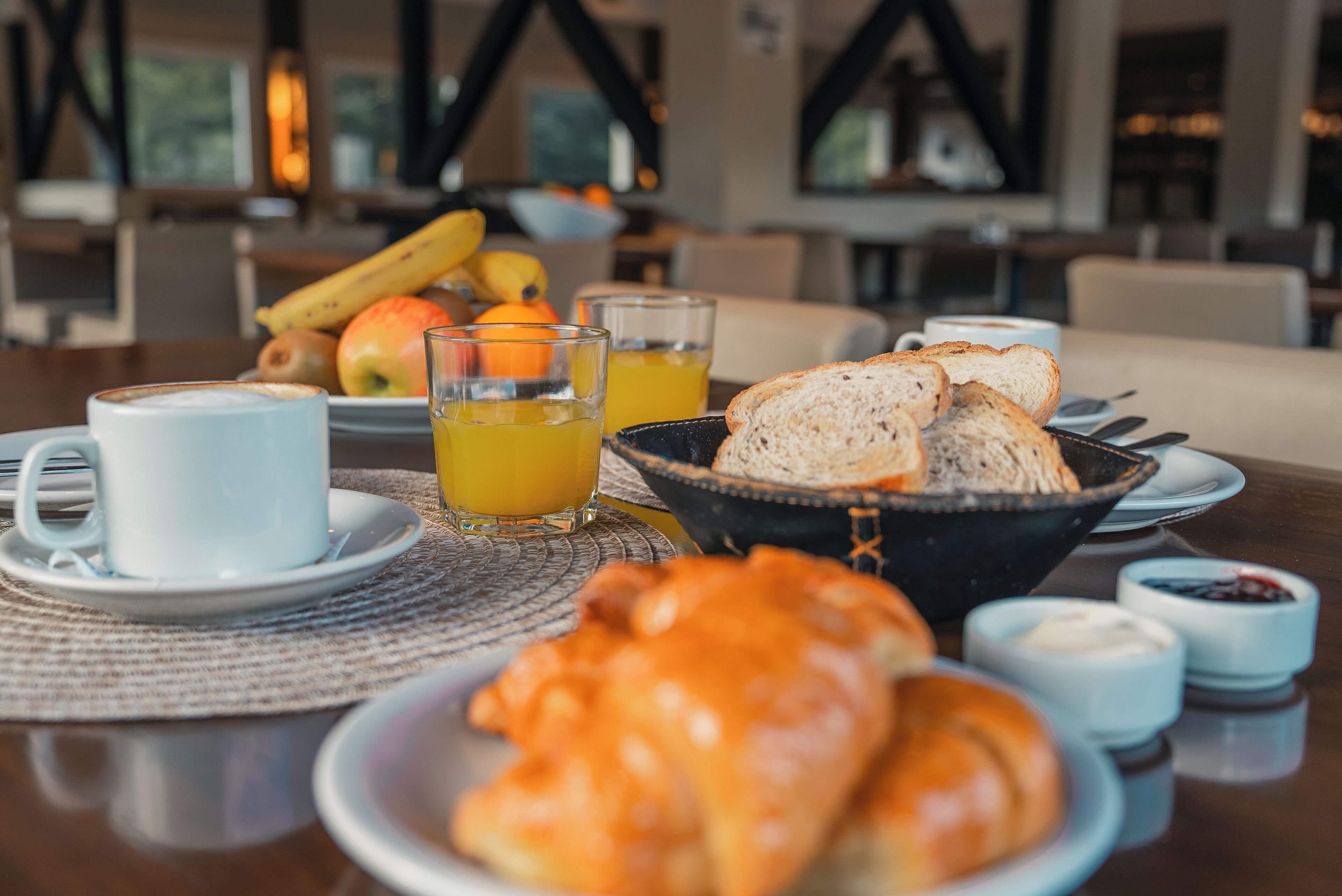 A breakfast setting with croissants, juice, and fruit on a table.