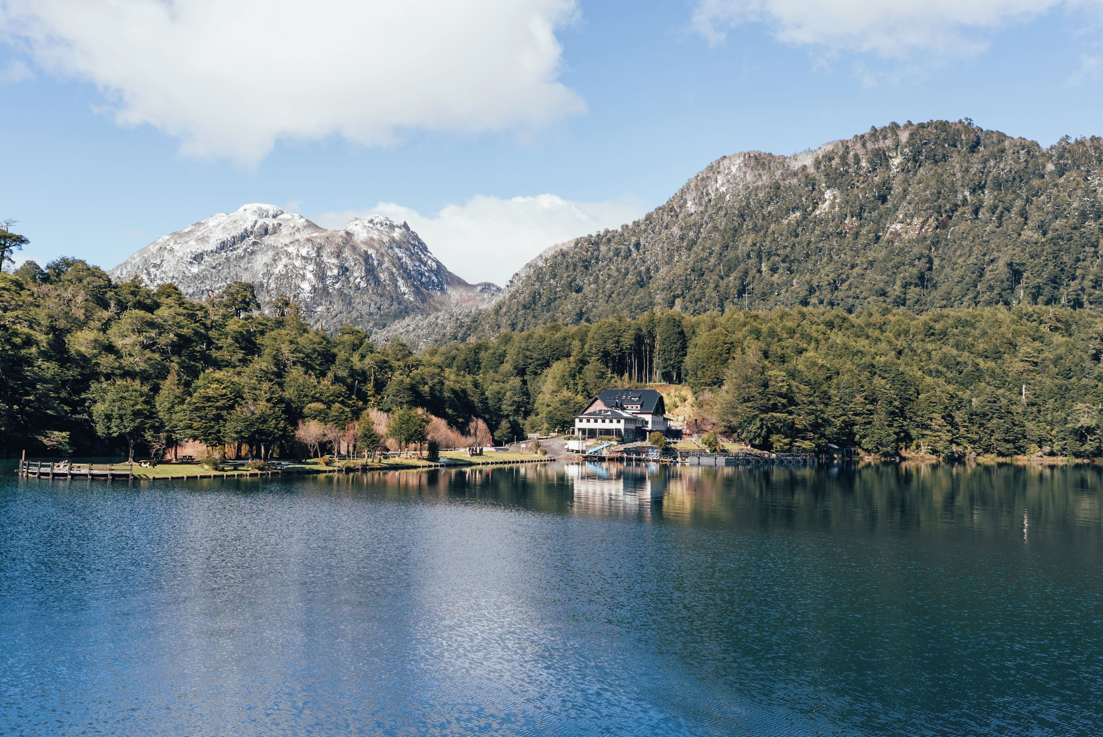 A lakeside property with a house surrounded by forested hills and a mountain in the background.