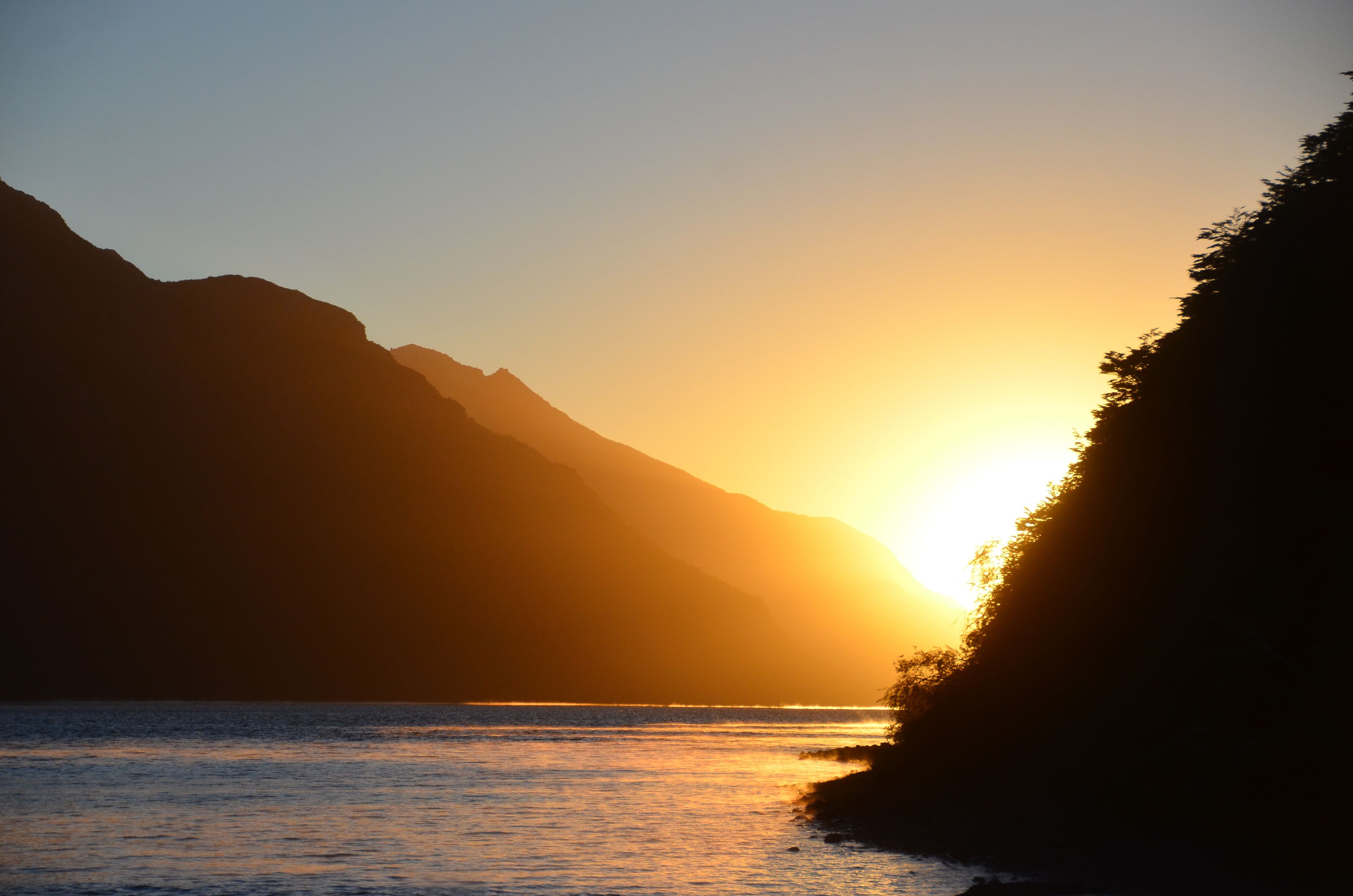Atardecer sobre una masa de agua con montañas al fondo.