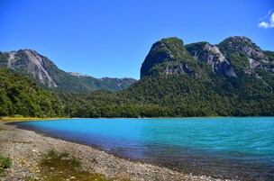 A serene lake with rocky shores and lush green mountains in the background.