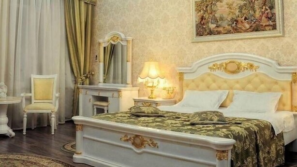 Un dormitorio clásico con una cama con dosel, una mesita de noche con lámpara, una silla y un cuadro en la pared.