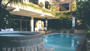Una piscina con hidromasaje, rodeada de plantas en macetas y una zona de estar cubierta.