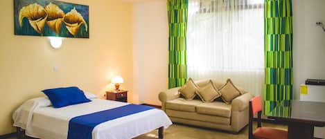 A hotel room with a bed, a sofa, a table, and a painting on the wall.