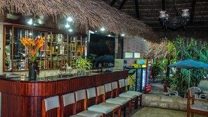 Zona de bar con techo de paja, barra de madera y asientos.