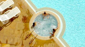 Uma banheira de hidromassagem cercada por uma piscina com espreguiçadeiras.