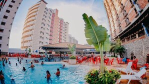 A swimming pool surrounded by red chairs and tables, with tall buildings in the background. - Villas Diroma Residence - BVTUR (Caldas Novas)