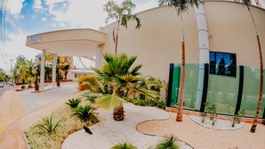 A gas station with a canopy, palm trees, and a paved area with plants. - Villas Diroma Residence - BVTUR (Caldas Novas)