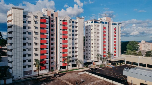 A multi-story residential building with balconies, a parking area, and a clear sky. - Villas Diroma Residence - BVTUR (Caldas Novas)