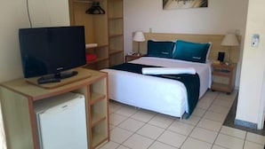A hotel room with a bed, a television, a wardrobe, and a small refrigerator. - Villas Diroma Residence - BVTUR (Caldas Novas)