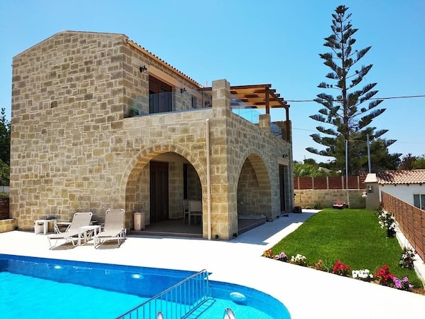 A stone building with a pool, outdoor seating, and a pergola.