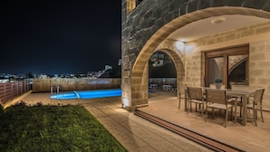 A rooftop pool area with stone arches, a dining area with chairs, and a view of the city at night. - Villa Katerina (Chania)
