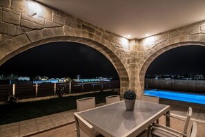 A stone archway leading to an outdoor patio with a pool, a table, and chairs.