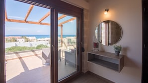 A modern interior with a sliding glass door leading to a balcony, a round mirror, and a small shelf with a plant. - Villa Katerina (Chania)