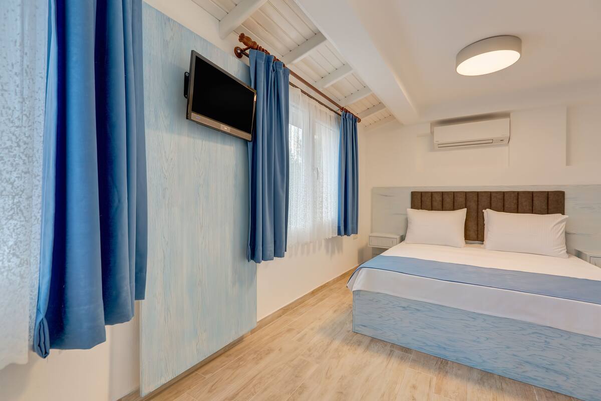 A modern hotel room with a large bed, a flat-screen TV mounted on the wall, and a ceiling fan.