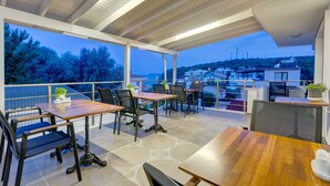 Un espacio de comedor al aire libre techado con mesas y sillas, con vistas a una colina pintoresca.