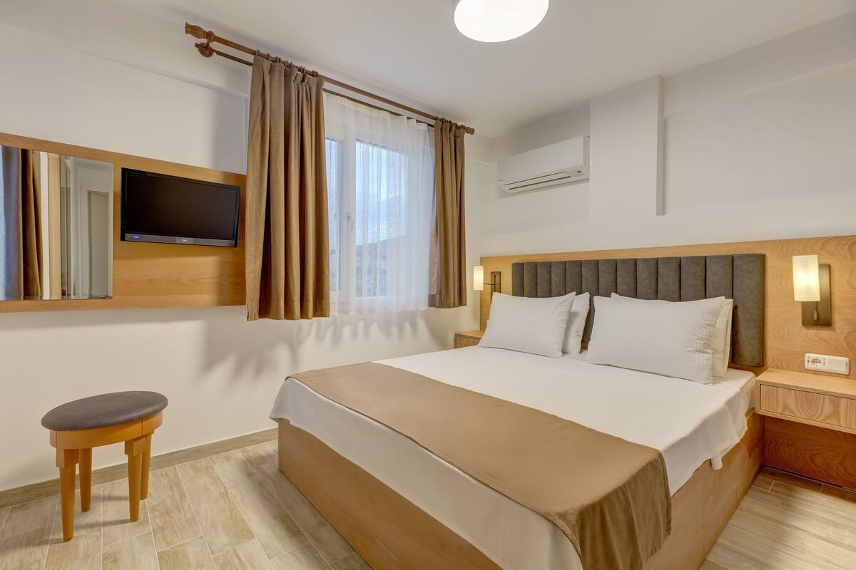 A hotel room with a large bed, a TV mounted on the wall, a bedside table, and a small stool.