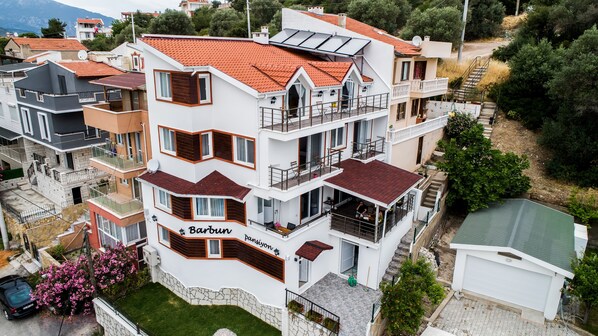 Un immeuble résidentiel à plusieurs étages, doté de balcons, d’une fondation en pierre et d’un toit recouvert de tuiles rouges.