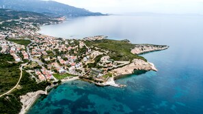 Vue aérienne d’une ville côtière avec des immeubles résidentiels, des eaux d’un bleu limpide et un paysage vallonné.