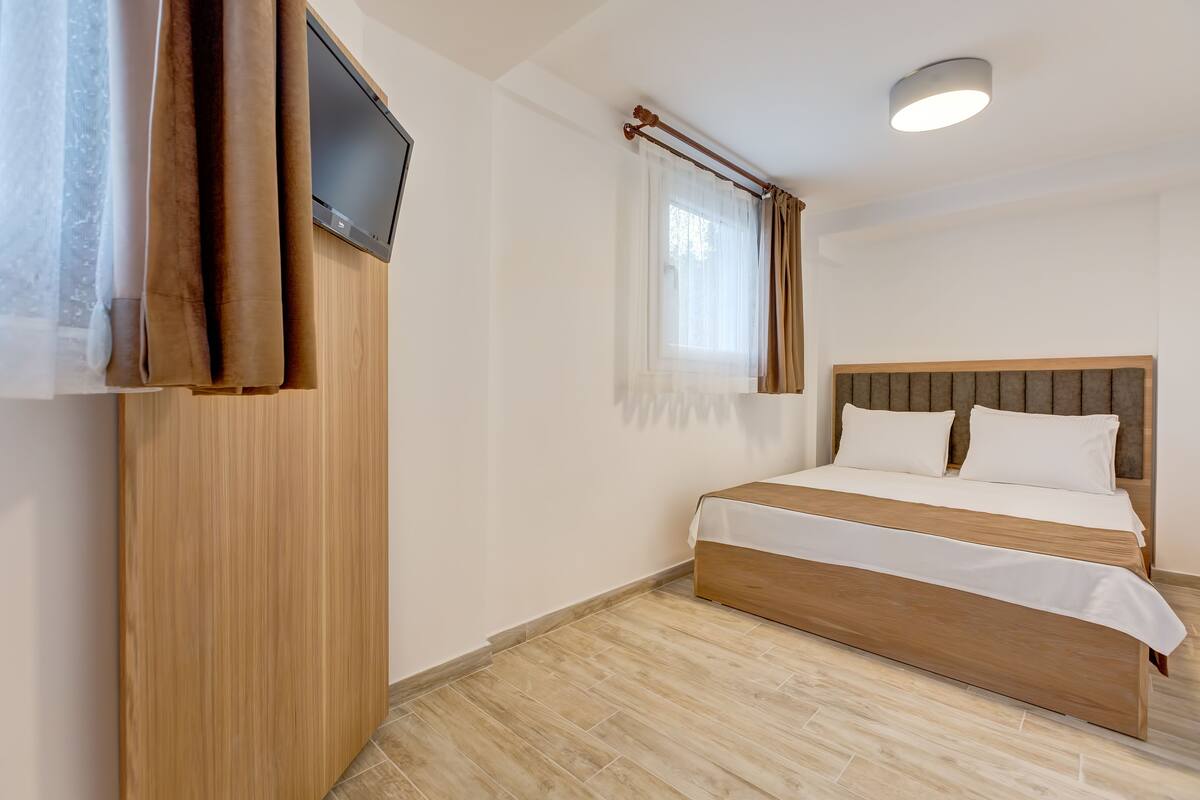 A bedroom with a wooden bed, a television mounted on the wall, and a window with curtains.