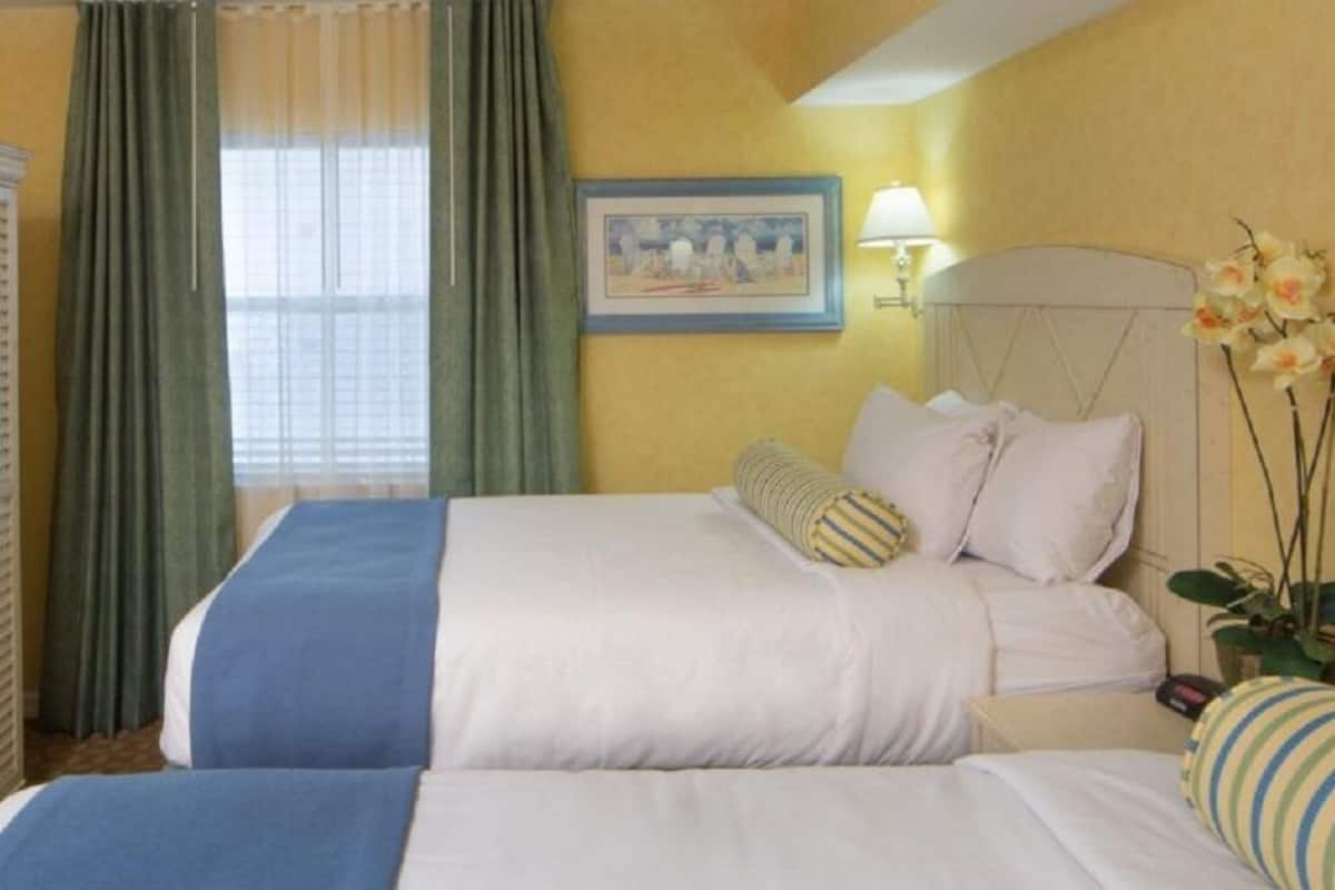 A hotel room with two beds, a television, a wardrobe, and a painting on the wall.