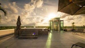 Terraço no telhado com elevador de vidro, área de estar externa e vista para a paisagem urbana.